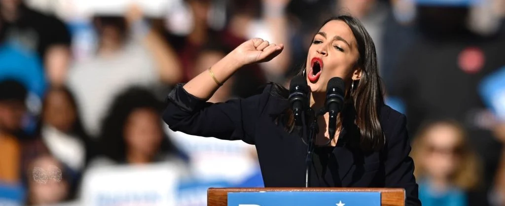 AOC giving some kind of speech somewhere. Uhm… I suddenly have the urge to draw something in her hand